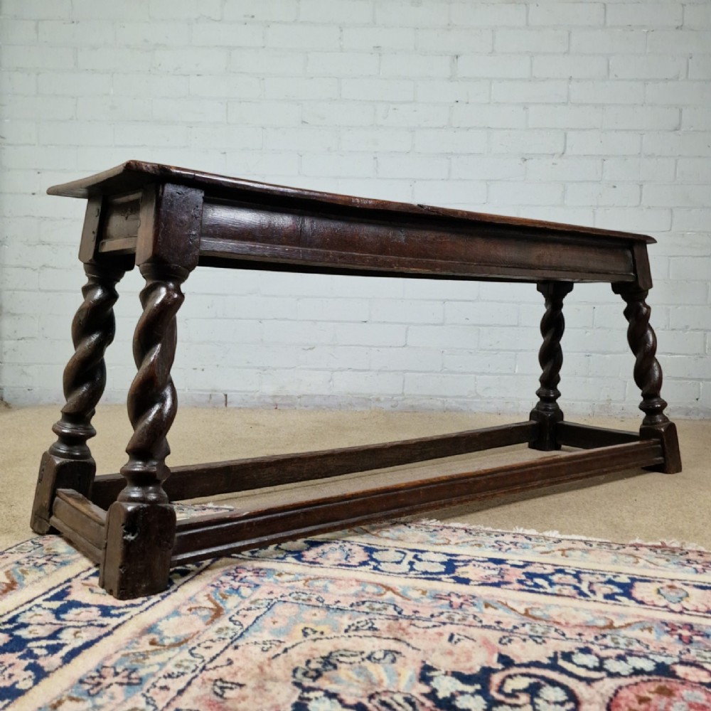 An 18th-century dark oak long stool featuring four barley twist legs connected by low stretchers beneath a solid rectangular top.