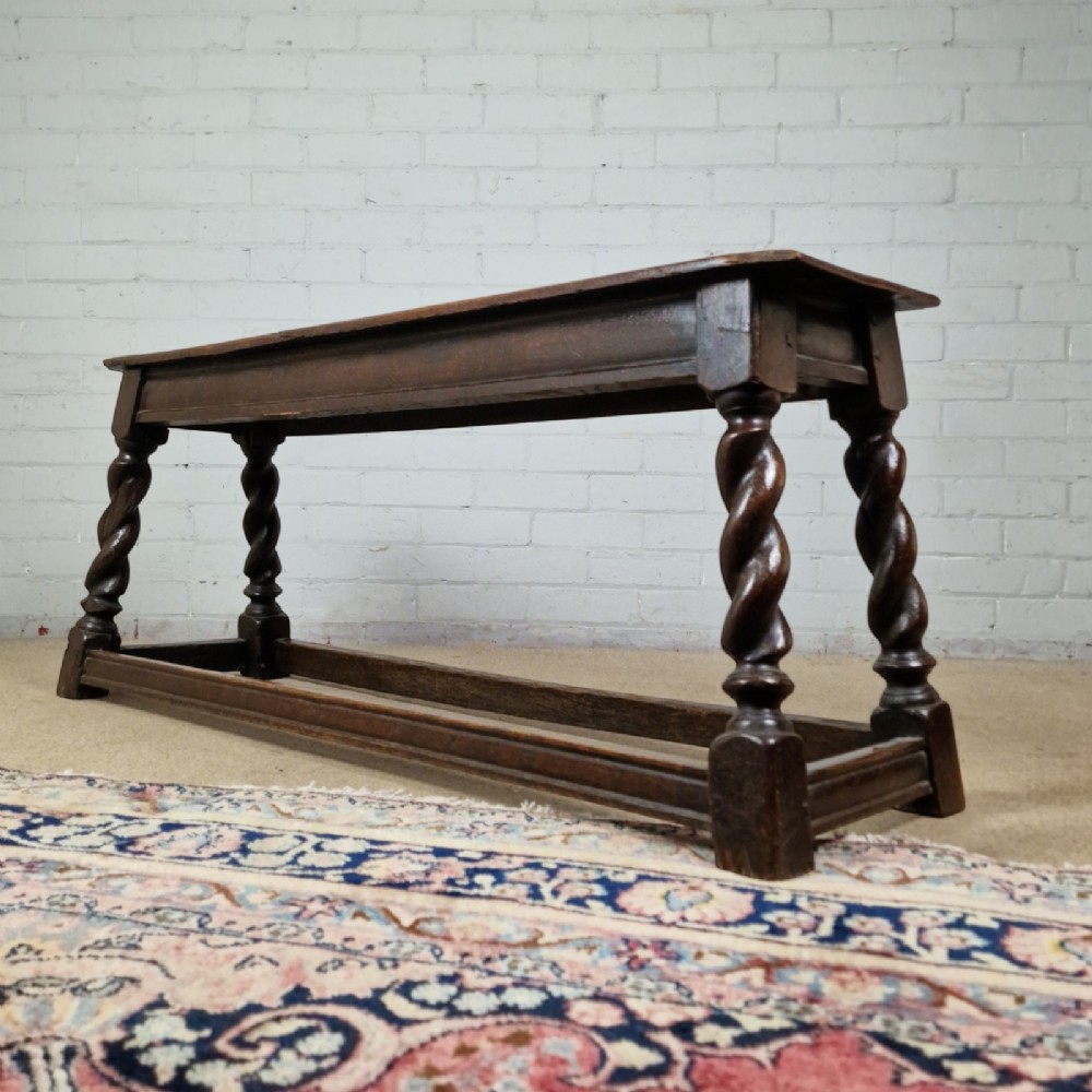 An 18th-century dark oak long stool featuring four barley twist legs connected by low stretchers beneath a solid rectangular top. View X