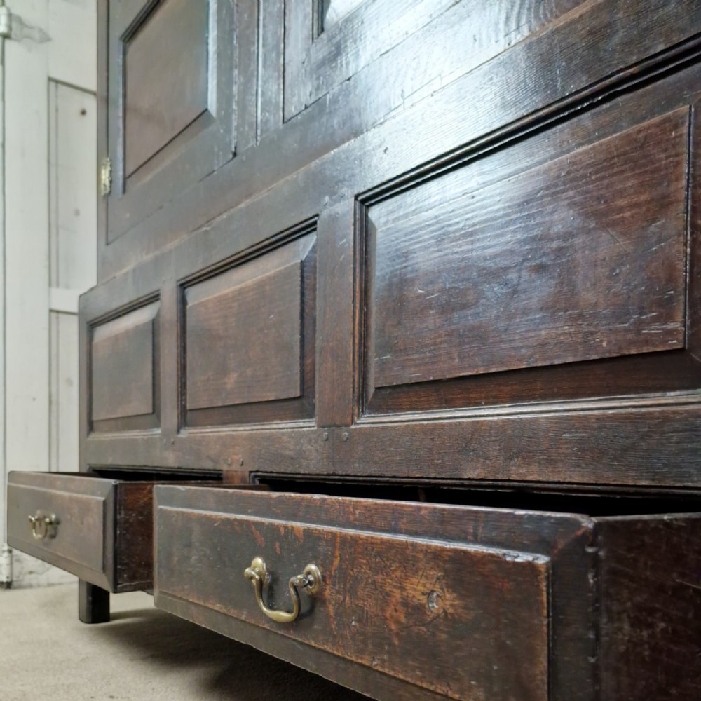 A mid-18th-century dark oak Georgian livery cupboard featuring raised panel doors, brass fittings, and lower drawers. View VI