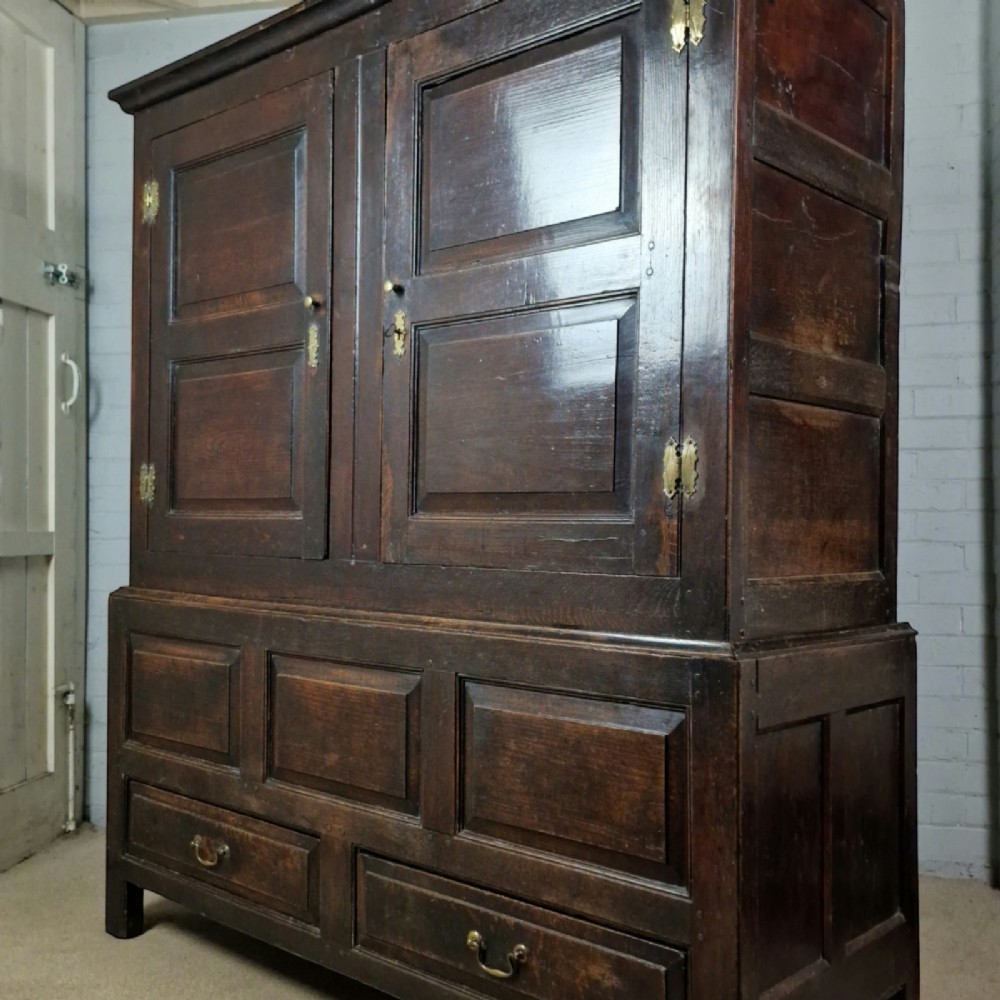 A mid-18th-century dark oak Georgian livery cupboard featuring raised panel doors, brass fittings, and lower drawers.
