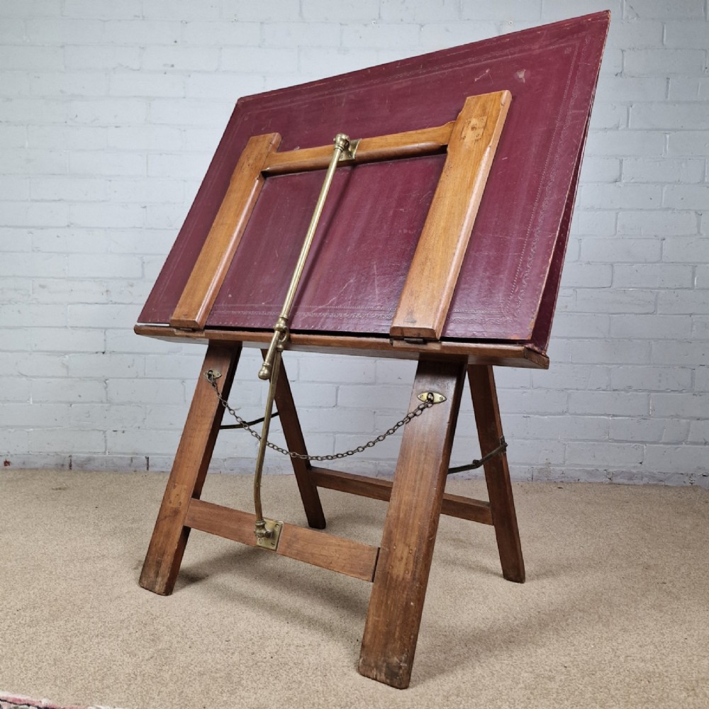A late 19th-century mahogany folio stand with burgundy leather panels, an adjustable brass ratchet arm, and a wooden trestle frame.