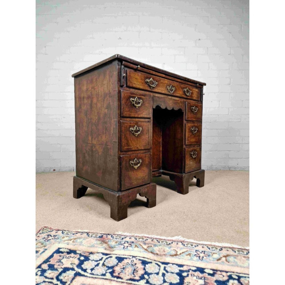 An early Georgian warm brown walnut kneehole desk featuring brass drop handles, side drawers, a central recessed cupboard, and bracket feet. View II