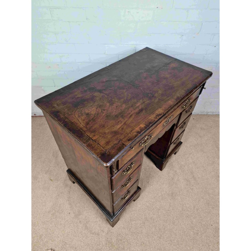 An early Georgian warm brown walnut kneehole desk featuring brass drop handles, side drawers, a central recessed cupboard, and bracket feet. View III