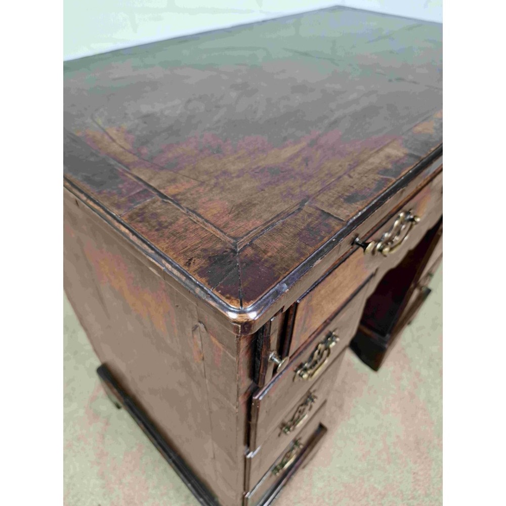 An early Georgian warm brown walnut kneehole desk featuring brass drop handles, side drawers, a central recessed cupboard, and bracket feet. View IV