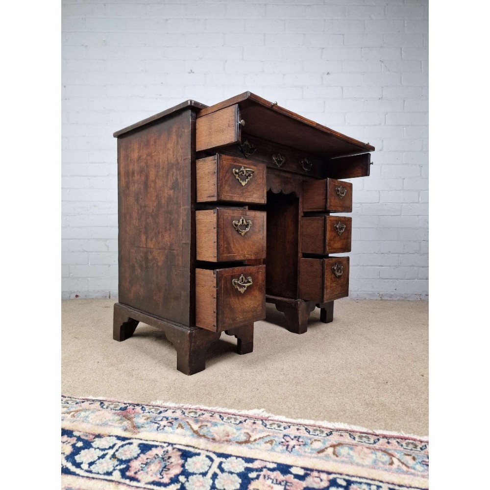 An early Georgian warm brown walnut kneehole desk featuring brass drop handles, side drawers, a central recessed cupboard, and bracket feet. View V