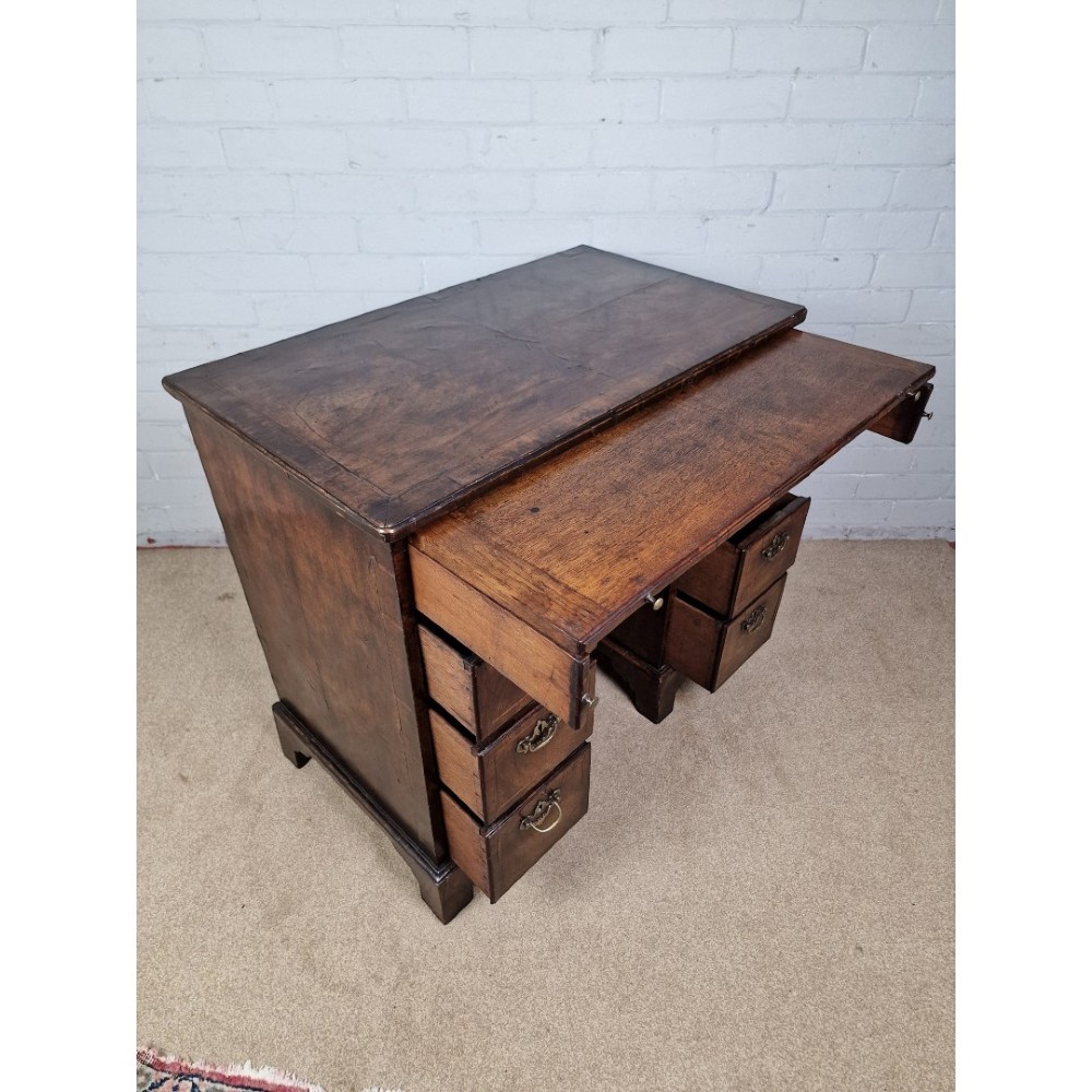 An early Georgian warm brown walnut kneehole desk featuring brass drop handles, side drawers, a central recessed cupboard, and bracket feet. View VI