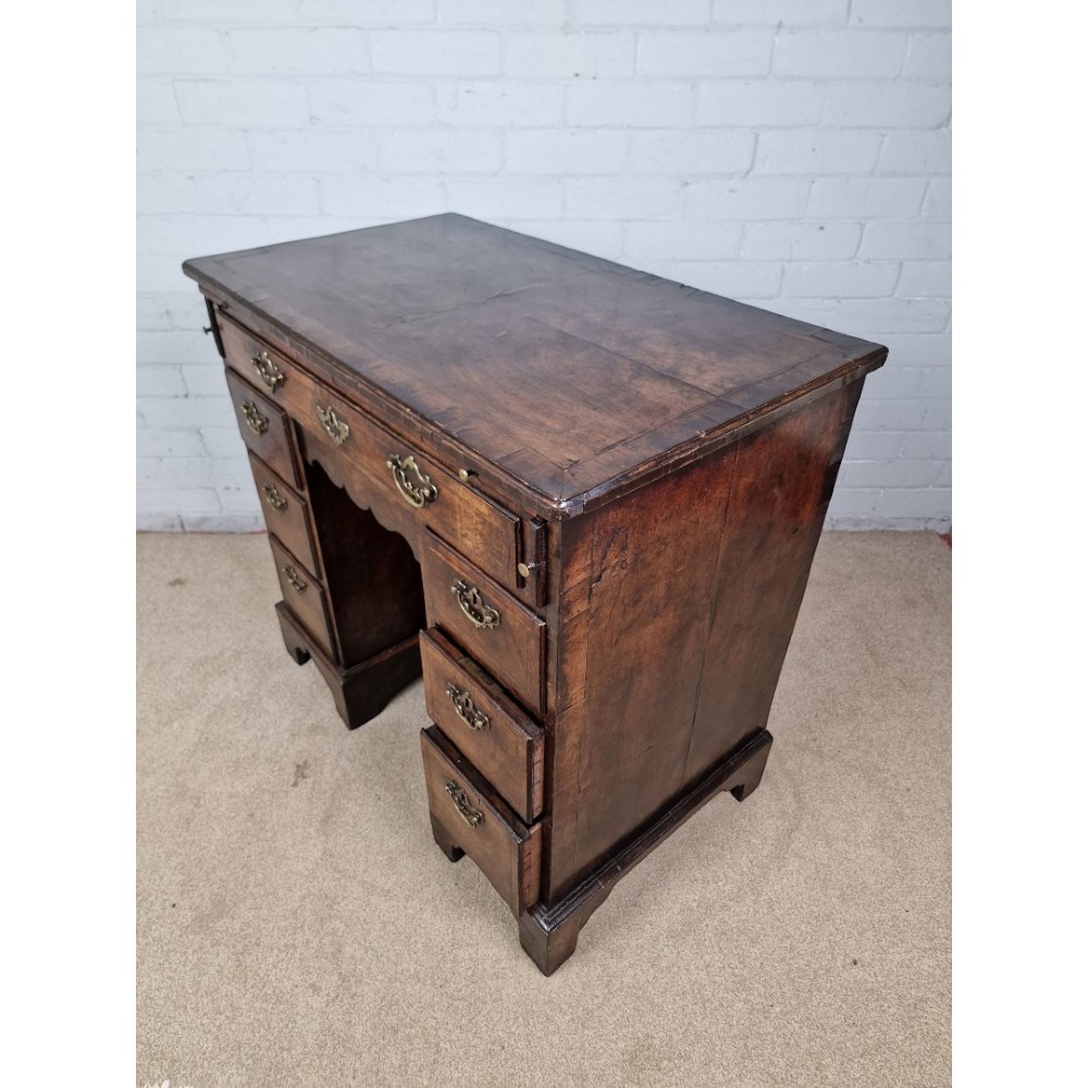 An early Georgian warm brown walnut kneehole desk featuring brass drop handles, side drawers, a central recessed cupboard, and bracket feet. View VIII