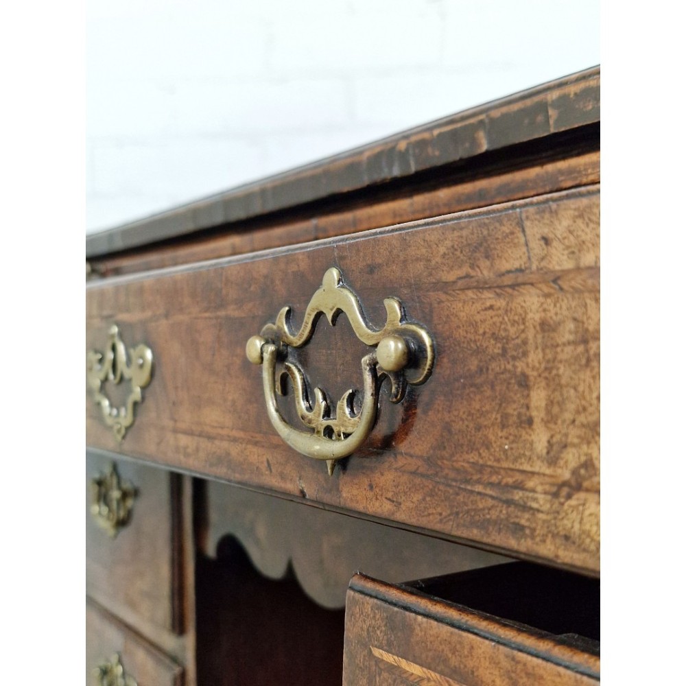 An early Georgian warm brown walnut kneehole desk featuring brass drop handles, side drawers, a central recessed cupboard, and bracket feet. View IX