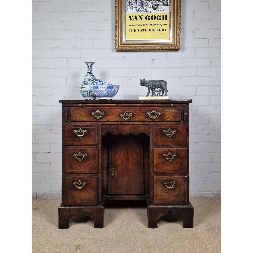 An early Georgian warm brown walnut kneehole desk featuring brass drop handles, side drawers, a central recessed cupboard, and bracket feet. View X