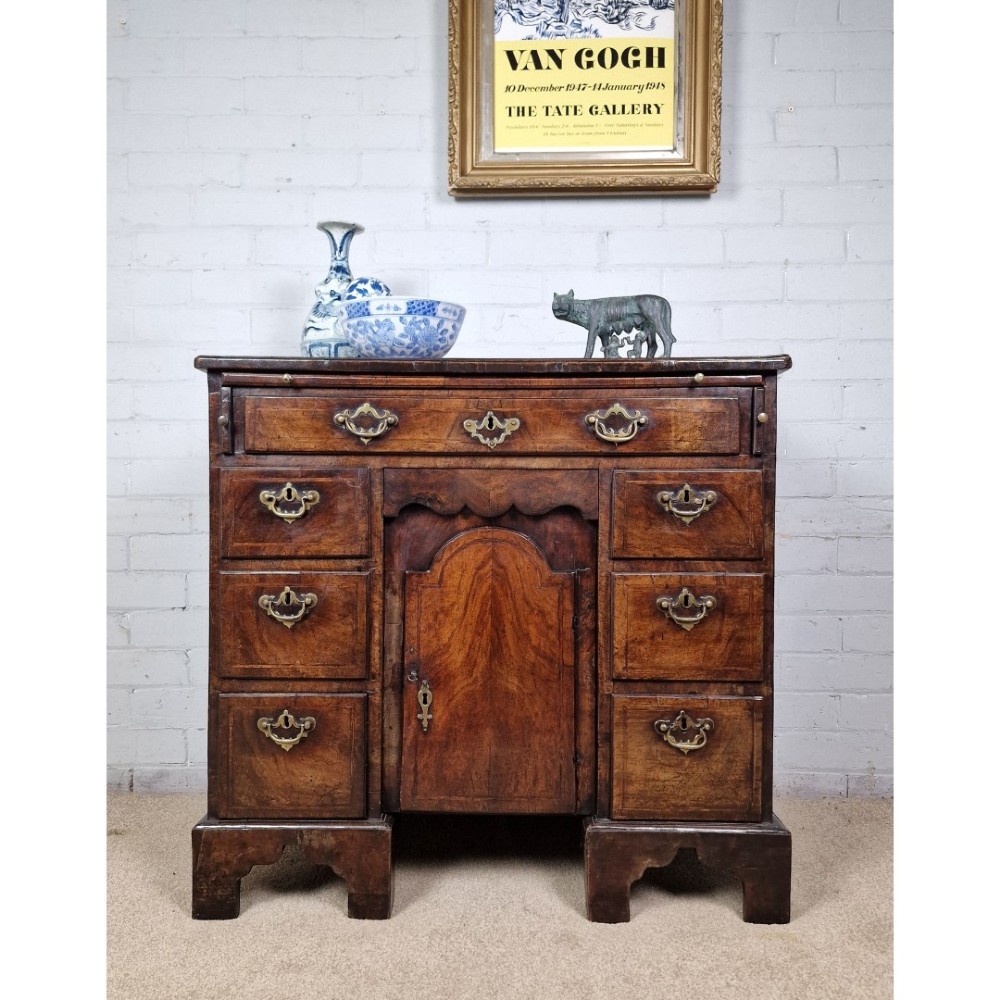 An early Georgian warm brown walnut kneehole desk featuring brass drop handles, side drawers, a central recessed cupboard, and bracket feet. View XI