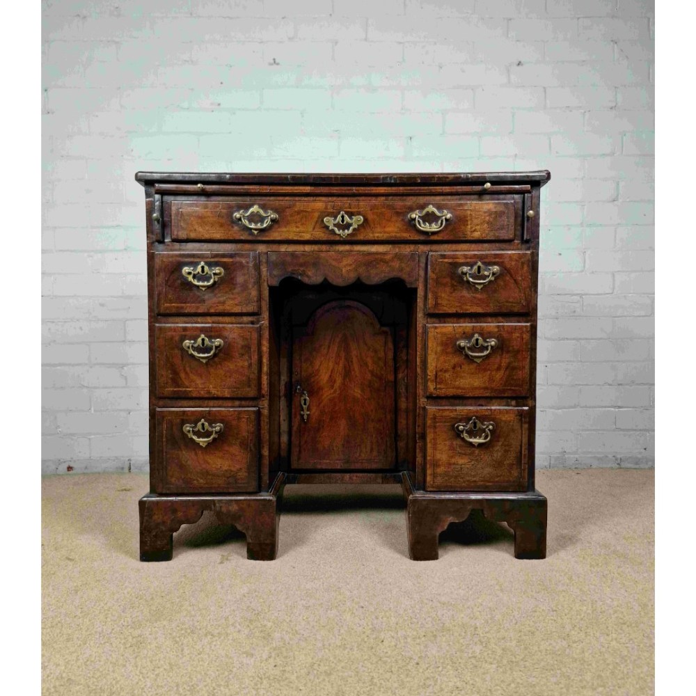 An early Georgian warm brown walnut kneehole desk featuring brass drop handles, side drawers, a central recessed cupboard, and bracket feet. View XII