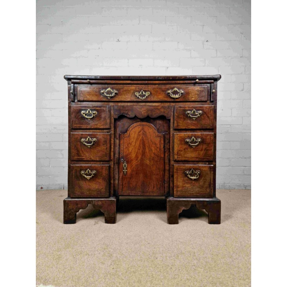 An early Georgian warm brown walnut kneehole desk featuring brass drop handles, side drawers, a central recessed cupboard, and bracket feet. View XIII