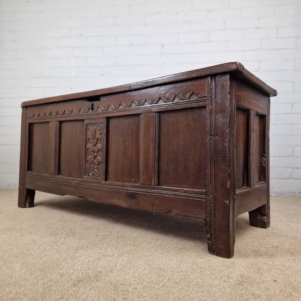 A seventeenth-century dark oak joined coffer featuring a carved central floral panel, a geometric top frieze, and a panelled front facade. View II