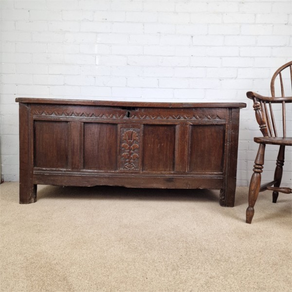 A seventeenth-century dark oak joined coffer featuring a carved central floral panel, a geometric top frieze, and a panelled front facade.
