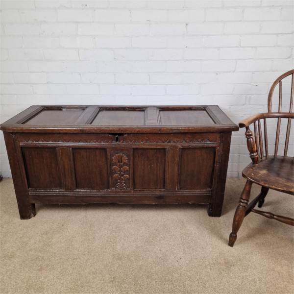 A seventeenth-century dark oak joined coffer featuring a carved central floral panel, a geometric top frieze, and a panelled front facade. View X
