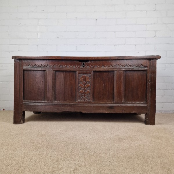 A seventeenth-century dark oak joined coffer featuring a carved central floral panel, a geometric top frieze, and a panelled front facade. View XI