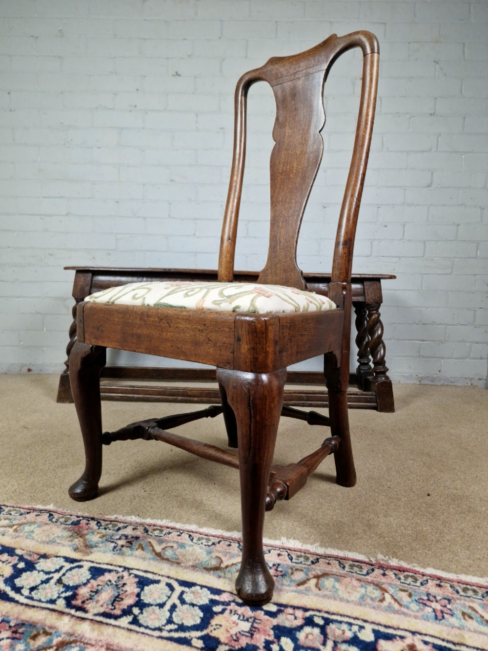 An early 18th century Queen Anne wooden dining chair featuring cabriole front legs, a vasiform back splat, and a patterned drop-in seat cushion. View IX