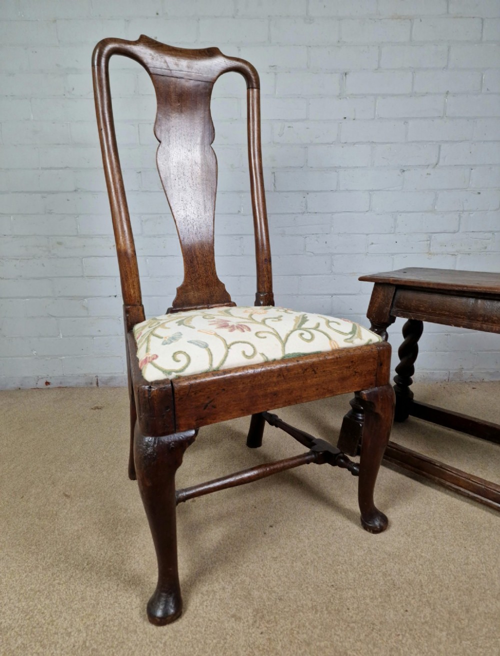 An early 18th century Queen Anne wooden dining chair featuring cabriole front legs, a vasiform back splat, and a patterned drop-in seat cushion. View X