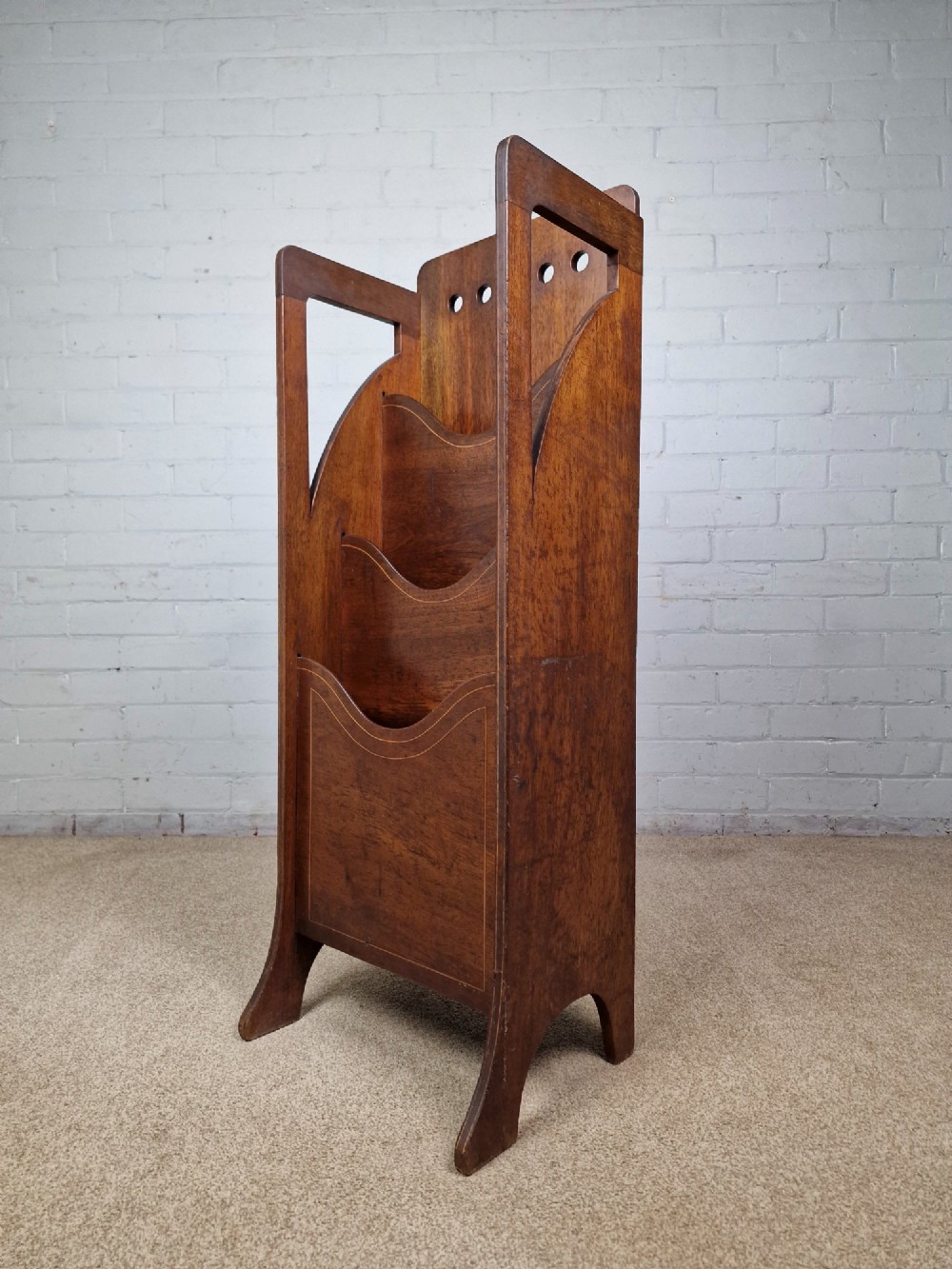 A tall Arts and Crafts brown oak magazine rack featuring three tiered compartments, circular cut-out details at the top, and integrated side carry handles. View III