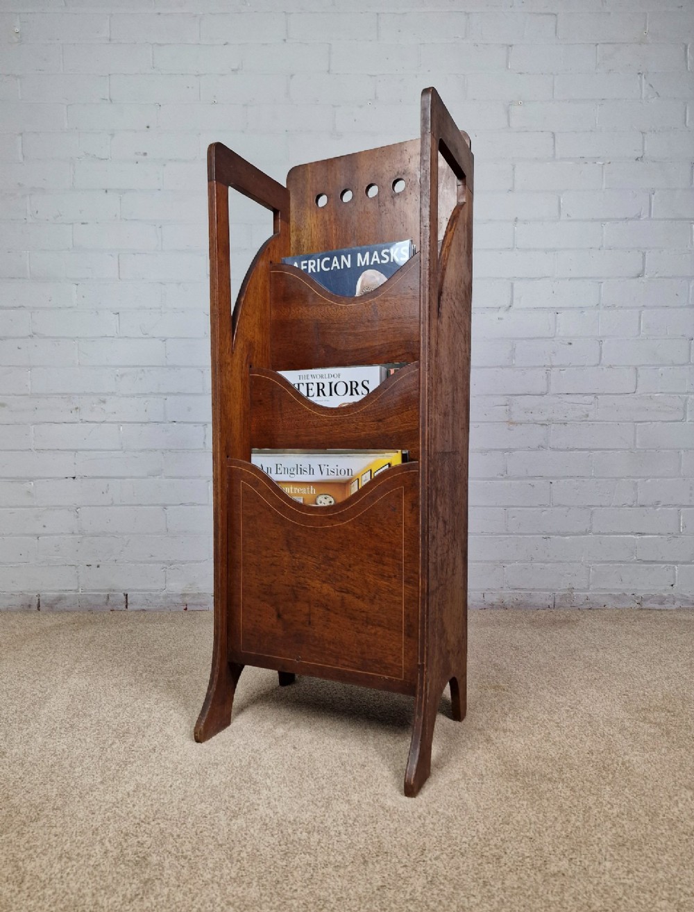 A tall Arts and Crafts brown oak magazine rack featuring three tiered compartments, circular cut-out details at the top, and integrated side carry handles.
