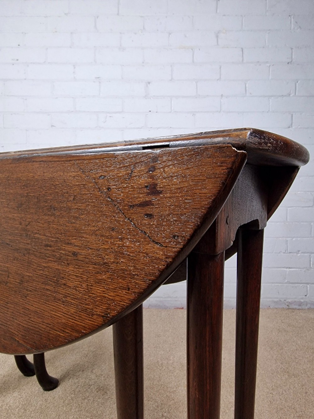 An 18th-century Georgian dark oak gateleg table with hinged leaves and slender tapered legs ending in pad feet. View VI