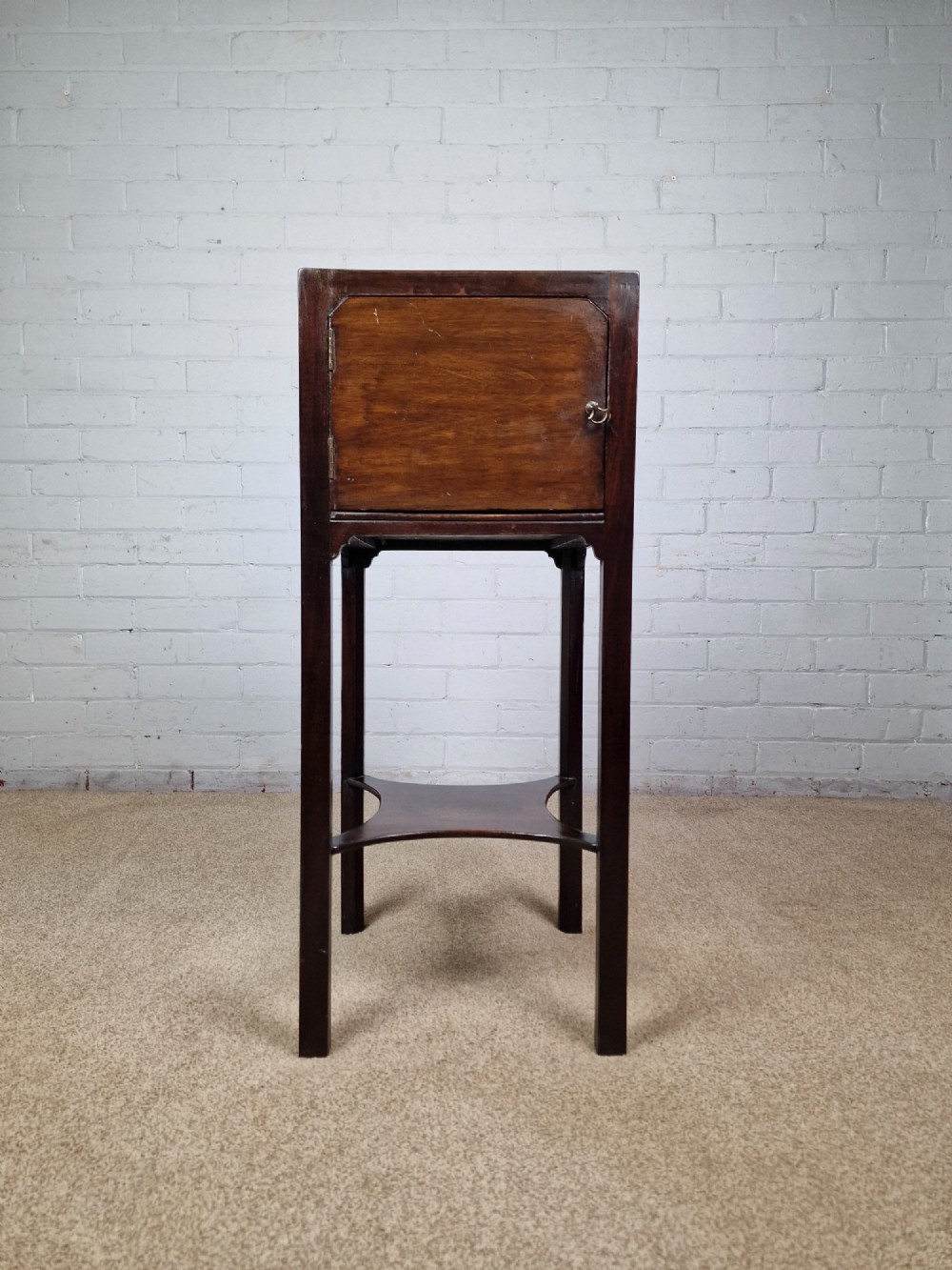 A tall Georgian dark mahogany bedside cabinet with a single door cupboard, straight legs, and an arched lower X-stretcher shelf.