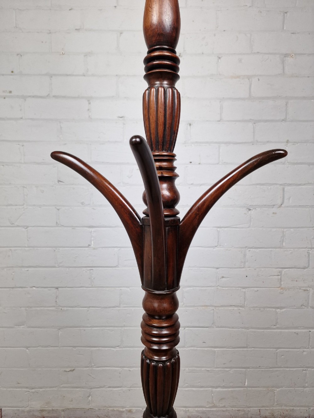 A tall late Georgian mahogany coat stand featuring turned and reeded central pillars, curved hanging hooks, and a splayed tripod base with brass castors. View II
