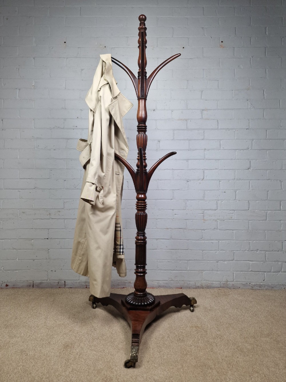 A tall late Georgian mahogany coat stand featuring turned and reeded central pillars, curved hanging hooks, and a splayed tripod base with brass castors.