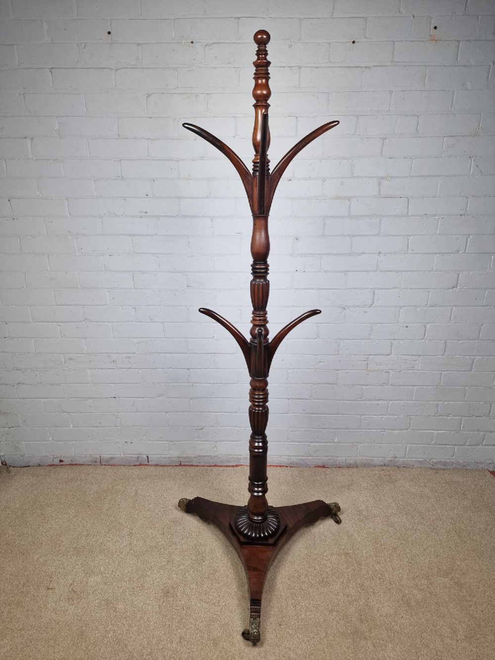 A tall late Georgian mahogany coat stand featuring turned and reeded central pillars, curved hanging hooks, and a splayed tripod base with brass castors. View VI