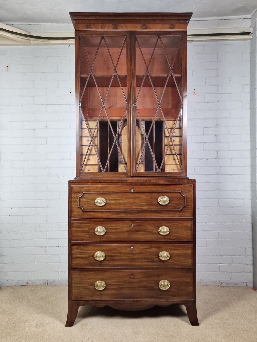 A George III mahogany secretaire bookcase featuring geometric astragal glazed upper doors above a lower chest of drawers with brass drop handles and bracket feet. View III