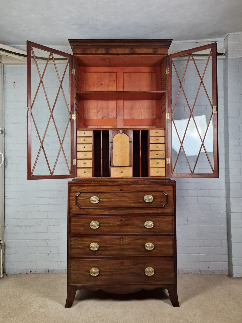 A George III mahogany secretaire bookcase featuring geometric astragal glazed upper doors above a lower chest of drawers with brass drop handles and bracket feet. View IV