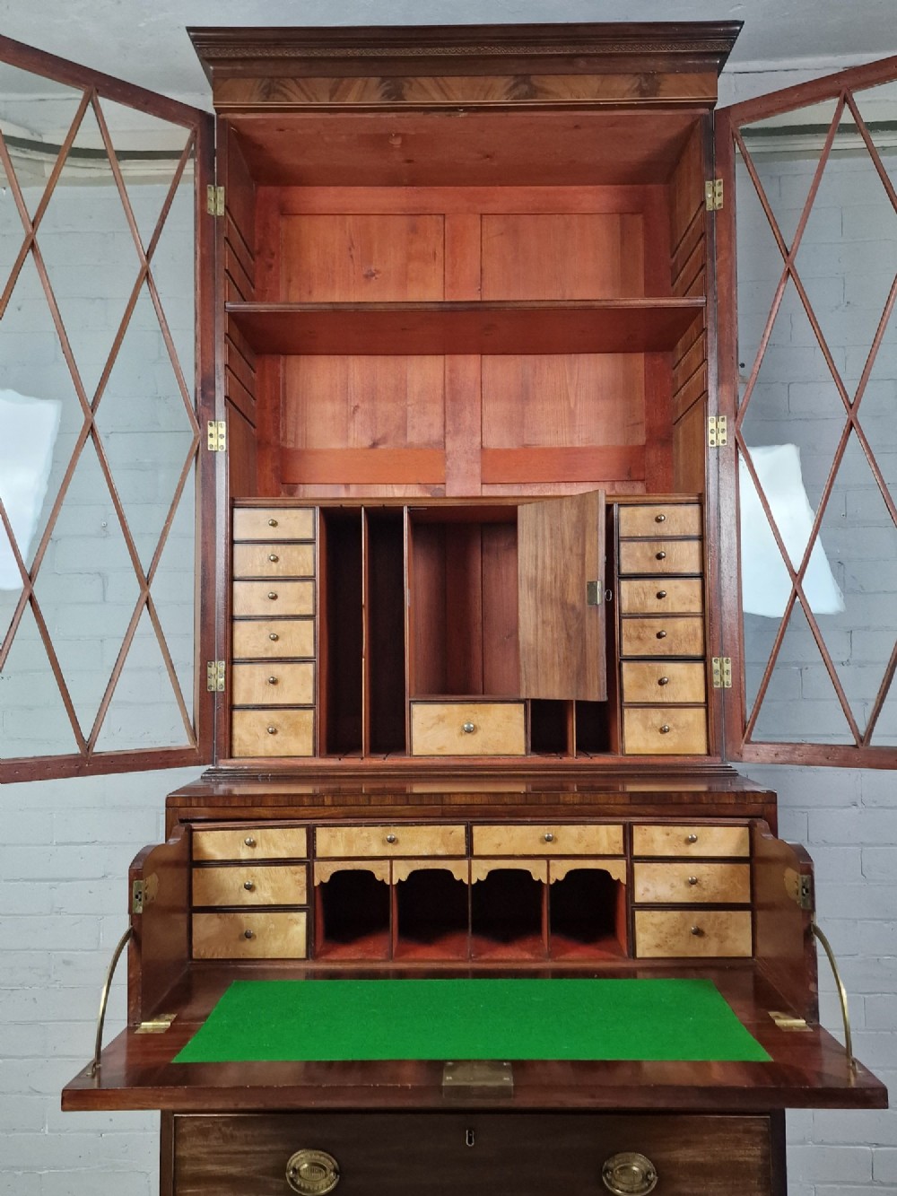 A George III mahogany secretaire bookcase featuring geometric astragal glazed upper doors above a lower chest of drawers with brass drop handles and bracket feet. View V