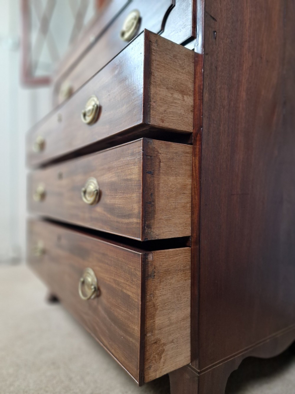 A George III mahogany secretaire bookcase featuring geometric astragal glazed upper doors above a lower chest of drawers with brass drop handles and bracket feet. View X