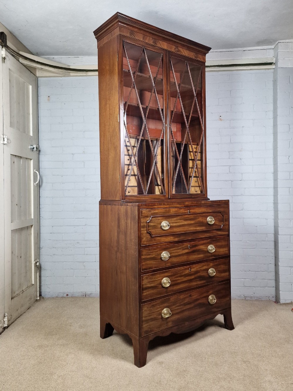 A George III mahogany secretaire bookcase featuring geometric astragal glazed upper doors above a lower chest of drawers with brass drop handles and bracket feet.