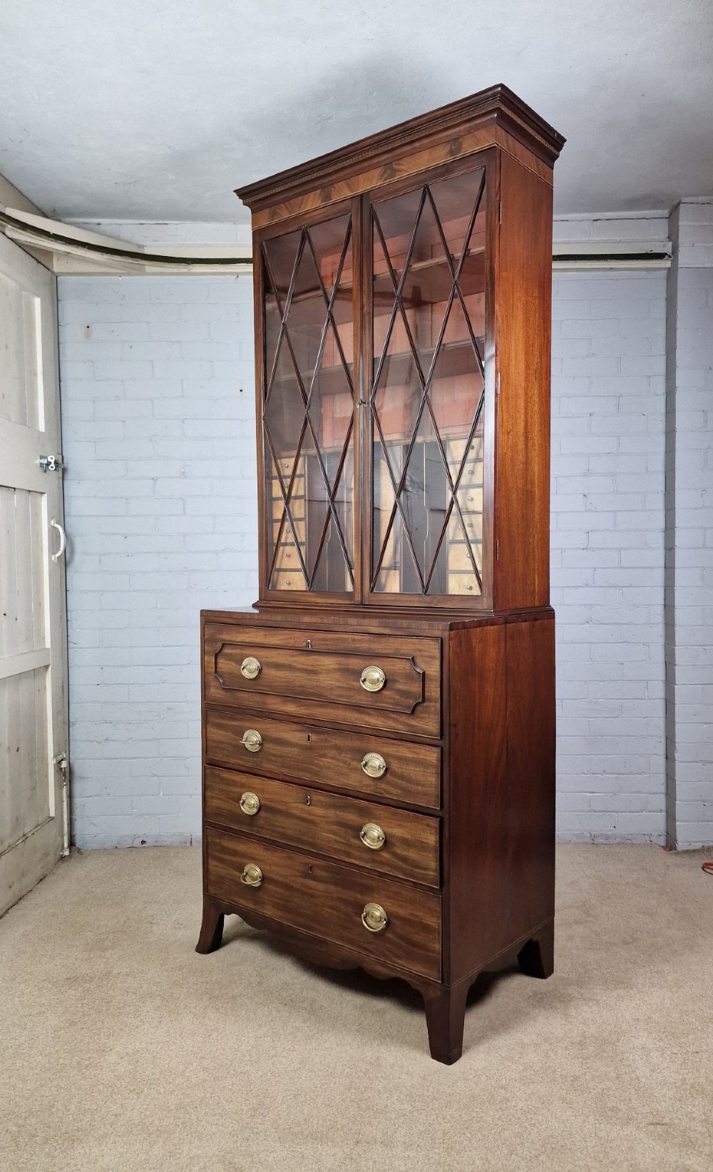 A George III mahogany secretaire bookcase featuring geometric astragal glazed upper doors above a lower chest of drawers with brass drop handles and bracket feet. View XII