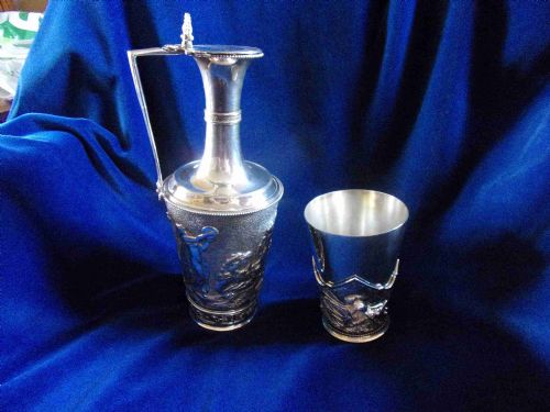 fig 1. A Victorian electrotype silver-plated wine jug with embossed classical figures alongside a matching silvered beaker.