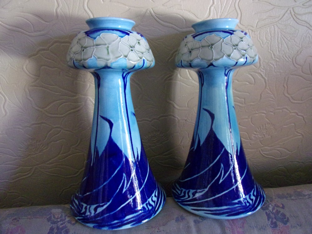 A pair of Edwardian Minton Secessionist earthenware vases with flared bases and bulbous rims, decorated with tube-lined floral and graphic wave motifs in shades of cobalt and sky blue.