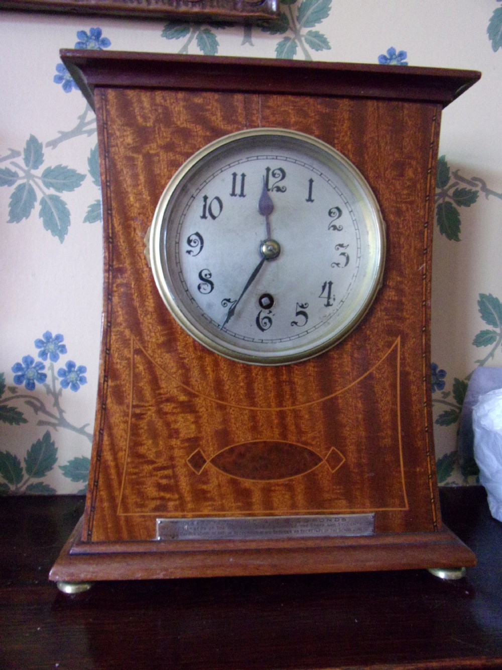 An Arts and Crafts Edwardian mahogany mantel clock featuring geometric line inlay, a circular white dial with Arabic numerals, and brass bun feet. View II