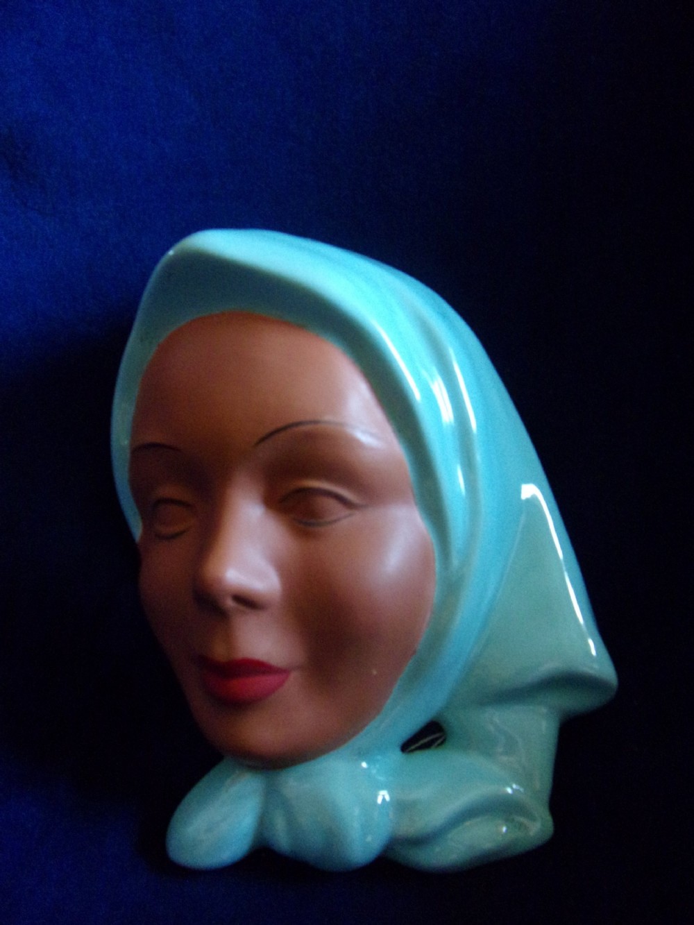 An Art Deco ceramic wall mask depicting a female face with matte terracotta skin and a glossy turquoise headscarf. View II