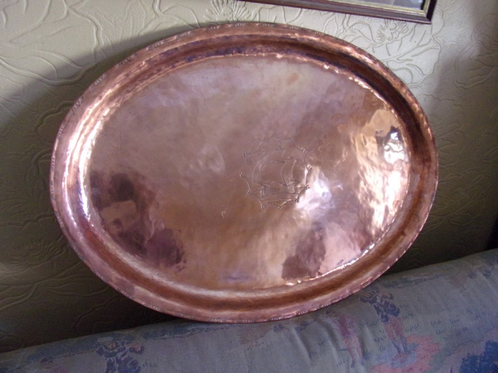 An oval Arts and Crafts copper tray featuring a hand-hammered surface texture, a raised border, and a central engraved sailing ship motif. View II