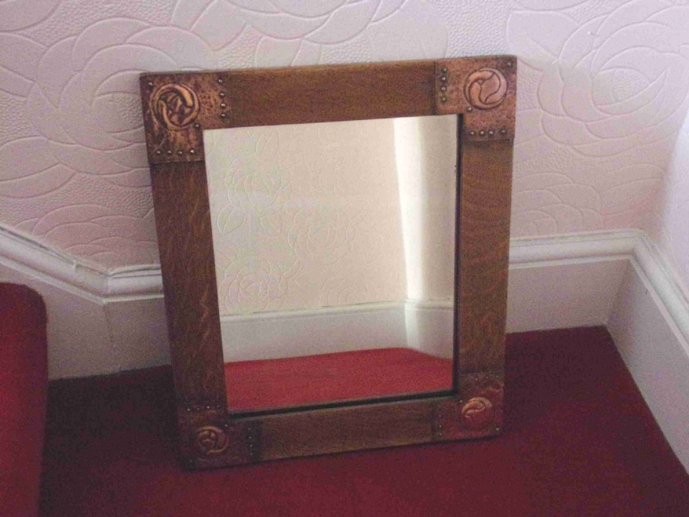 A rectangular oak wall mirror featuring corner plates of hand-worked repousse copper with Celtic knot motifs.