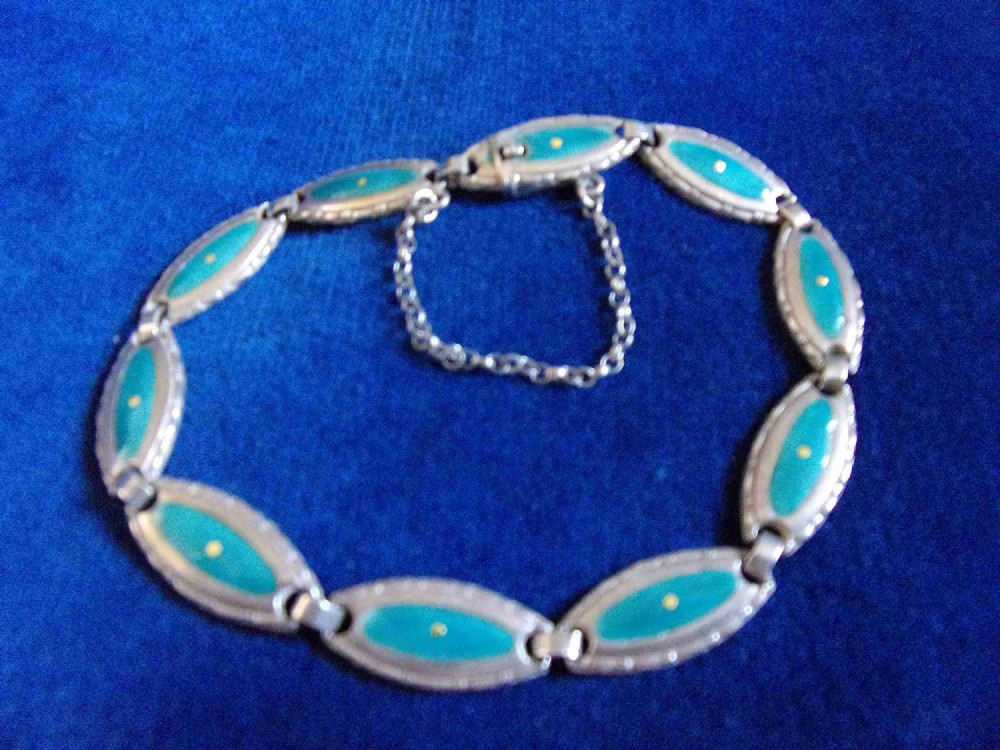 An Arts and Crafts sterling silver link bracelet featuring oval panels inset with green enamel and central yellow accents, complete with a safety chain.