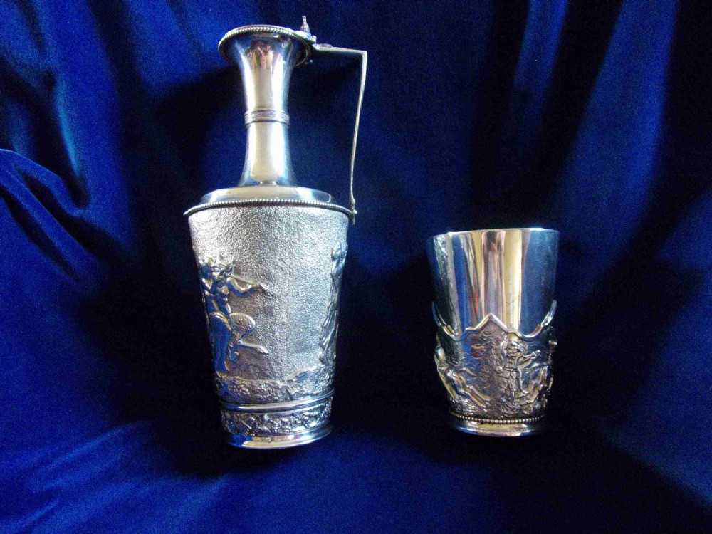 A Victorian electrotype silver-plated wine jug with embossed classical figures alongside a matching silvered beaker.