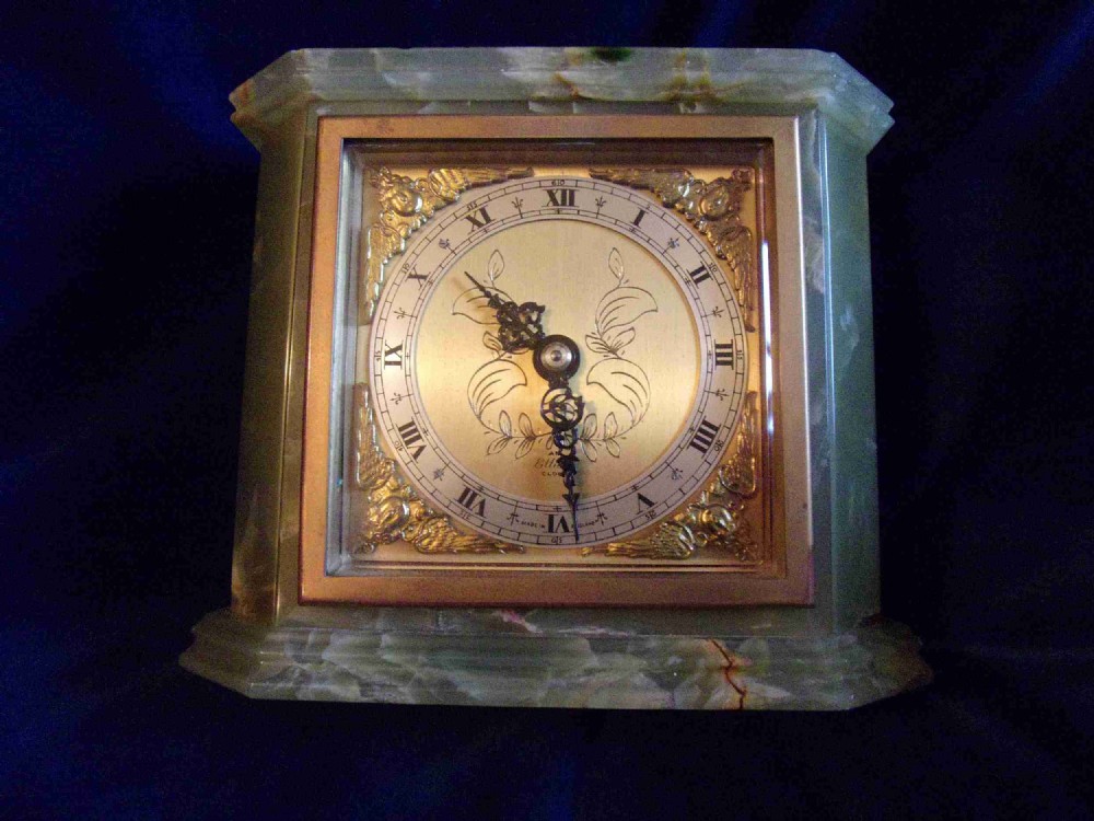 An Art Deco green onyx mantel clock featuring a square brass dial with Roman numerals and ornate corner spandrels.