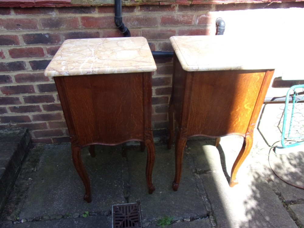 A pair of French oak bedside cabinets featuring mottled beige marble tops, single drawers, cupboard doors with carved raised panels, and slender cabriole legs. View V