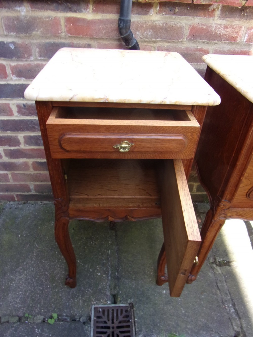 A pair of French oak bedside cabinets featuring mottled beige marble tops, single drawers, cupboard doors with carved raised panels, and slender cabriole legs. View IV