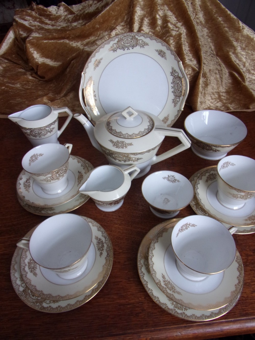 An eighteen piece cream and white porcelain tea set with gold floral gilded rims, comprising teacups, saucers, a teapot, milk pitchers, and a circular serving plate.