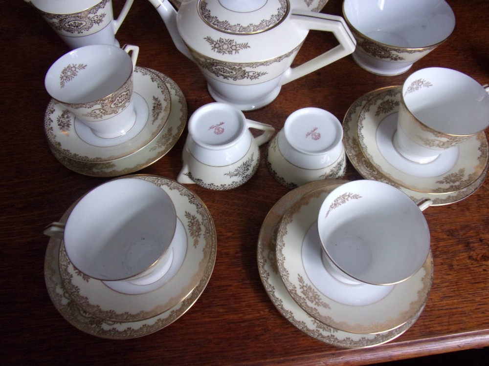 An eighteen piece cream and white porcelain tea set with gold floral gilded rims, comprising teacups, saucers, a teapot, milk pitchers, and a circular serving plate. View II