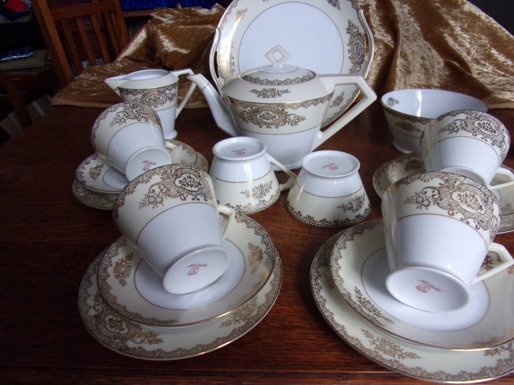 An eighteen piece cream and white porcelain tea set with gold floral gilded rims, comprising teacups, saucers, a teapot, milk pitchers, and a circular serving plate. View III