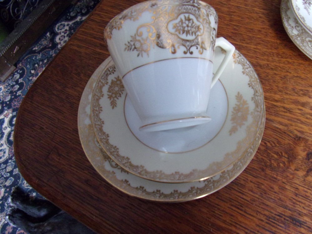 An eighteen piece cream and white porcelain tea set with gold floral gilded rims, comprising teacups, saucers, a teapot, milk pitchers, and a circular serving plate. View IV